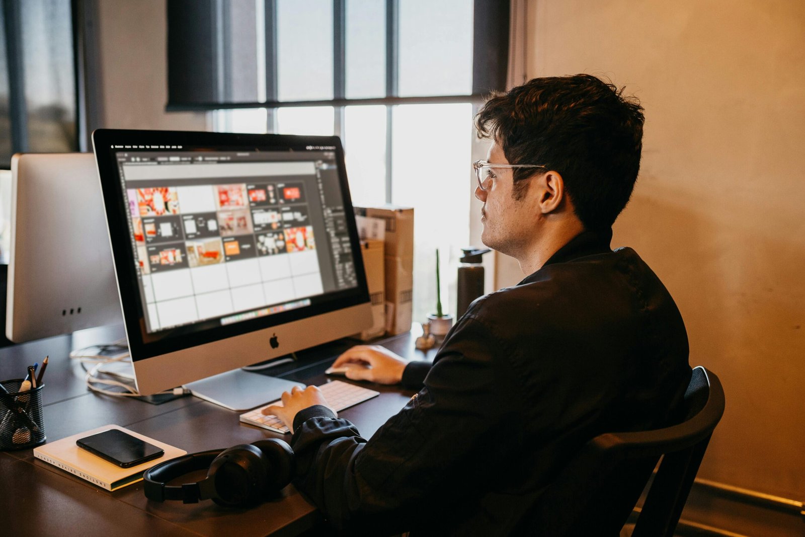 Man using a computer for graphic design work in a modern office setting with natural lighting.